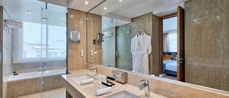 A modern bathroom with a large mirror, two sinks, a glass-enclosed shower, and a view of the city.