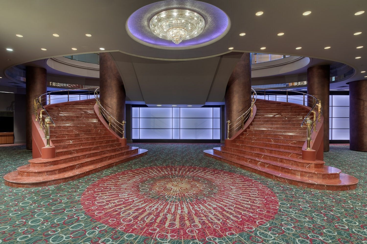Una imponente escalera con diseño de alfombra circular que conduce a un moderno vestíbulo con una lámpara de techo de diseño único.