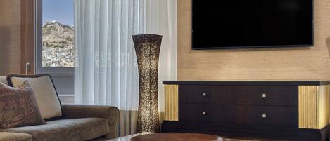 A modern living room with a sofa, a coffee table with a decorative bowl, a tall vase, and a flat-screen TV mounted on the wall.