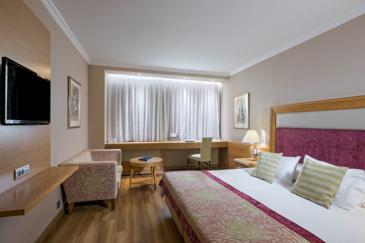 A hotel room with a bed, a desk, a chair, a TV, and a window with curtains.