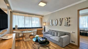 Een moderne woonkamer met een bank, een glazen salontafel en een televisie. Op de muur staat een groot 'LOVE'-bord en op een bijzettafeltje staat een lamp.
