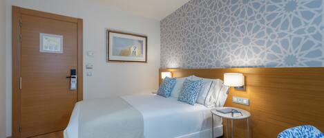 A hotel room with a bed, bedside table, chair, and a patterned wall.