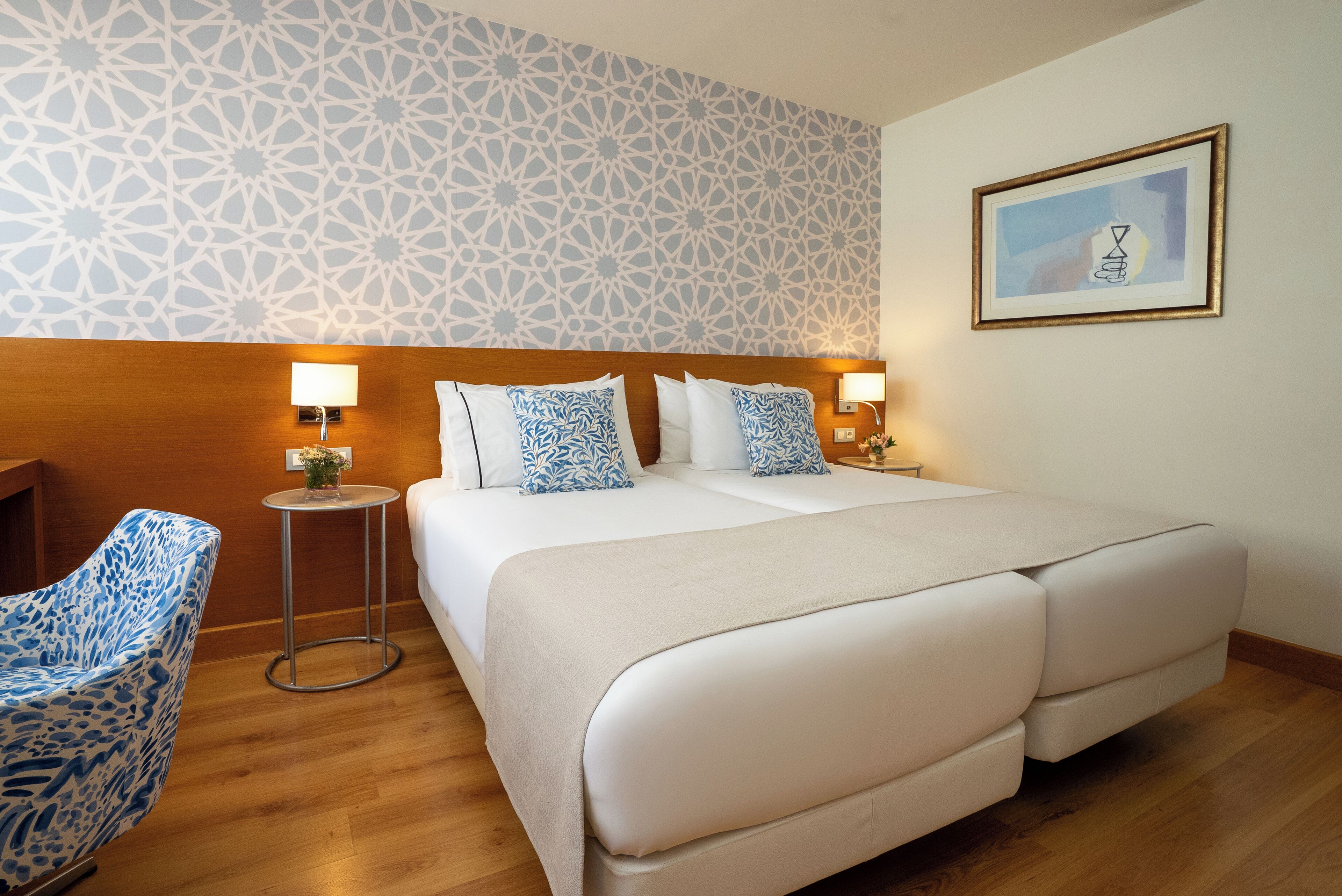 A hotel room with a large bed, two bedside tables with lamps, a patterned wall, and a framed picture on the wall.