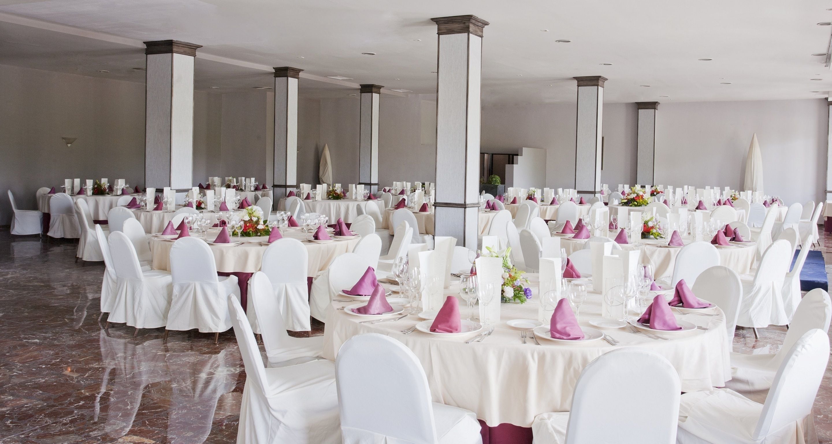 A banquet hall with round tables, white chairs, and purple napkins.
