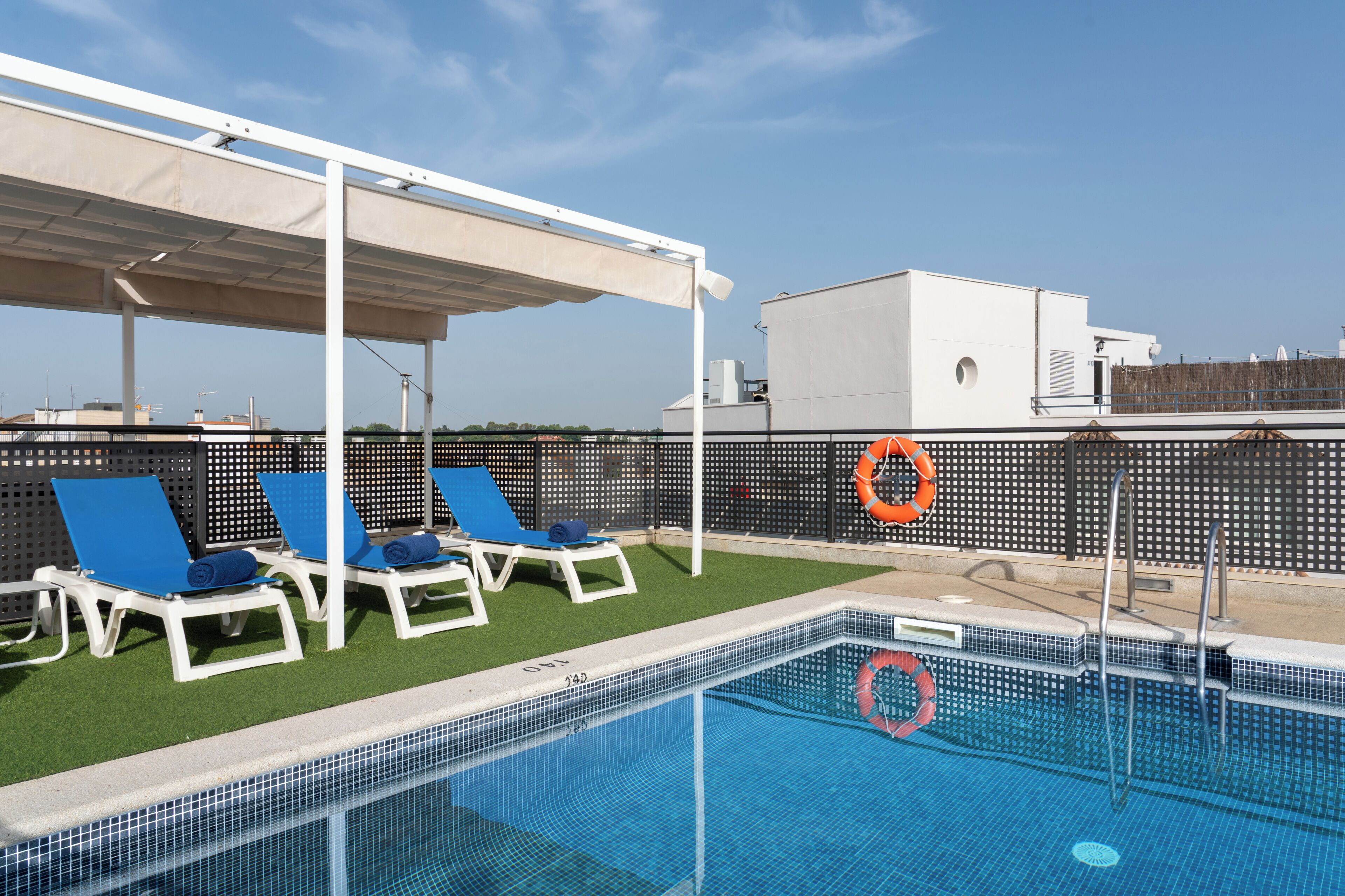 Un espace piscine aménagé sur le toit, avec des chaises longues bleues, un coin salon abrité et des bouées de sauvetage.