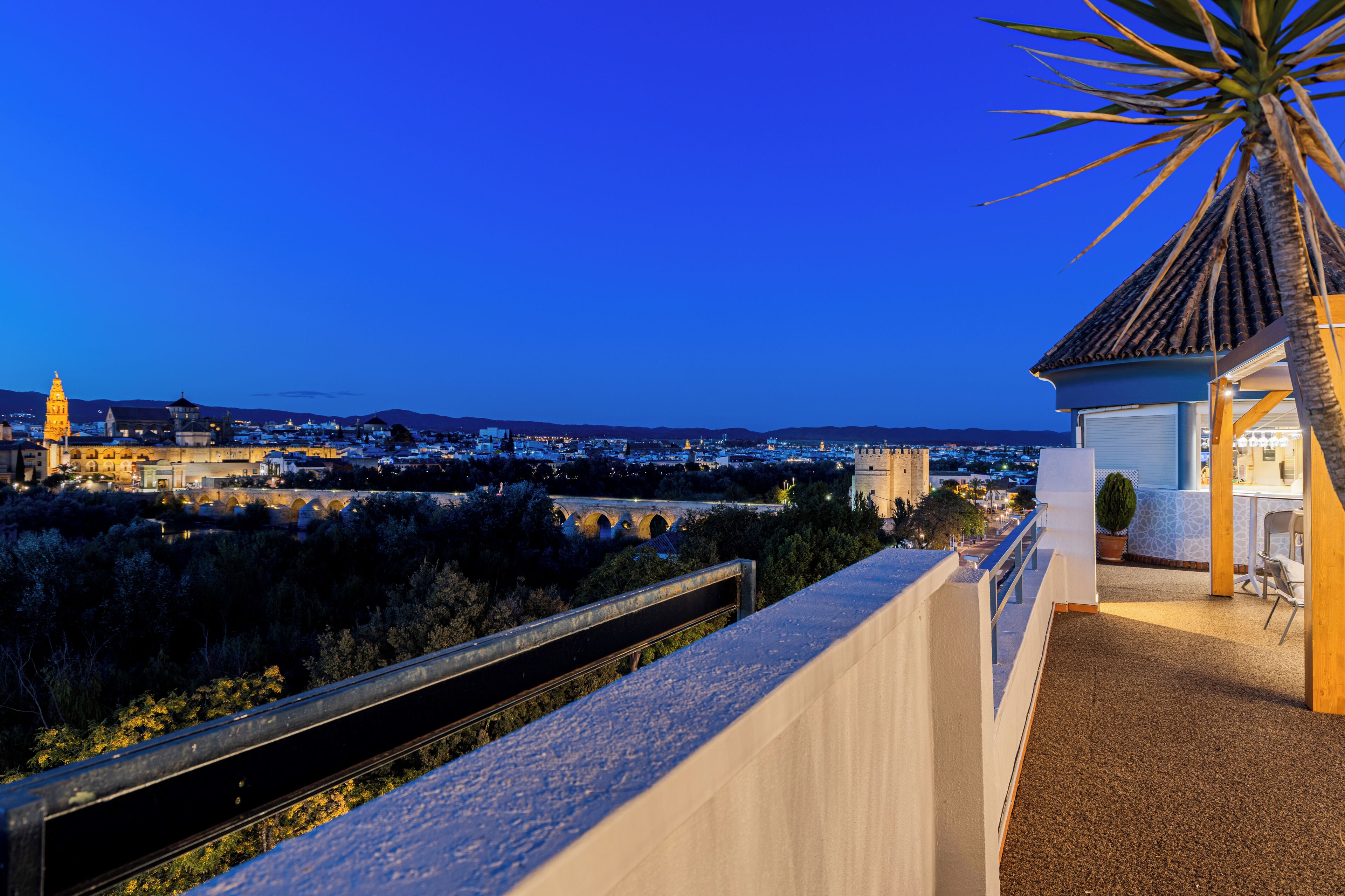 A balcony with a view of a cityscape at dusk, including a tower and a bridge.