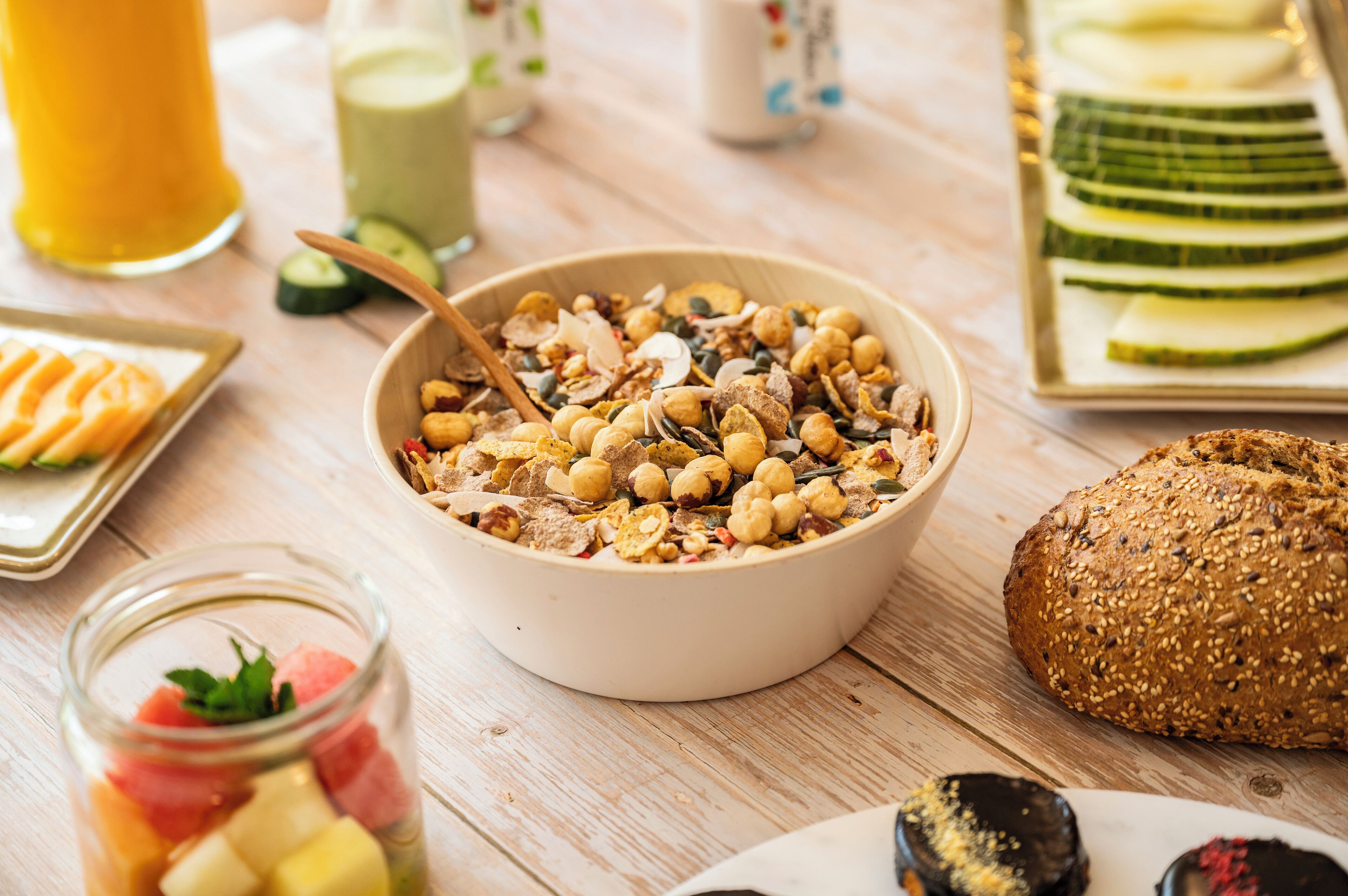 A breakfast setting with a bowl of cereal, a loaf of bread, and a plate of sliced cucumbers.