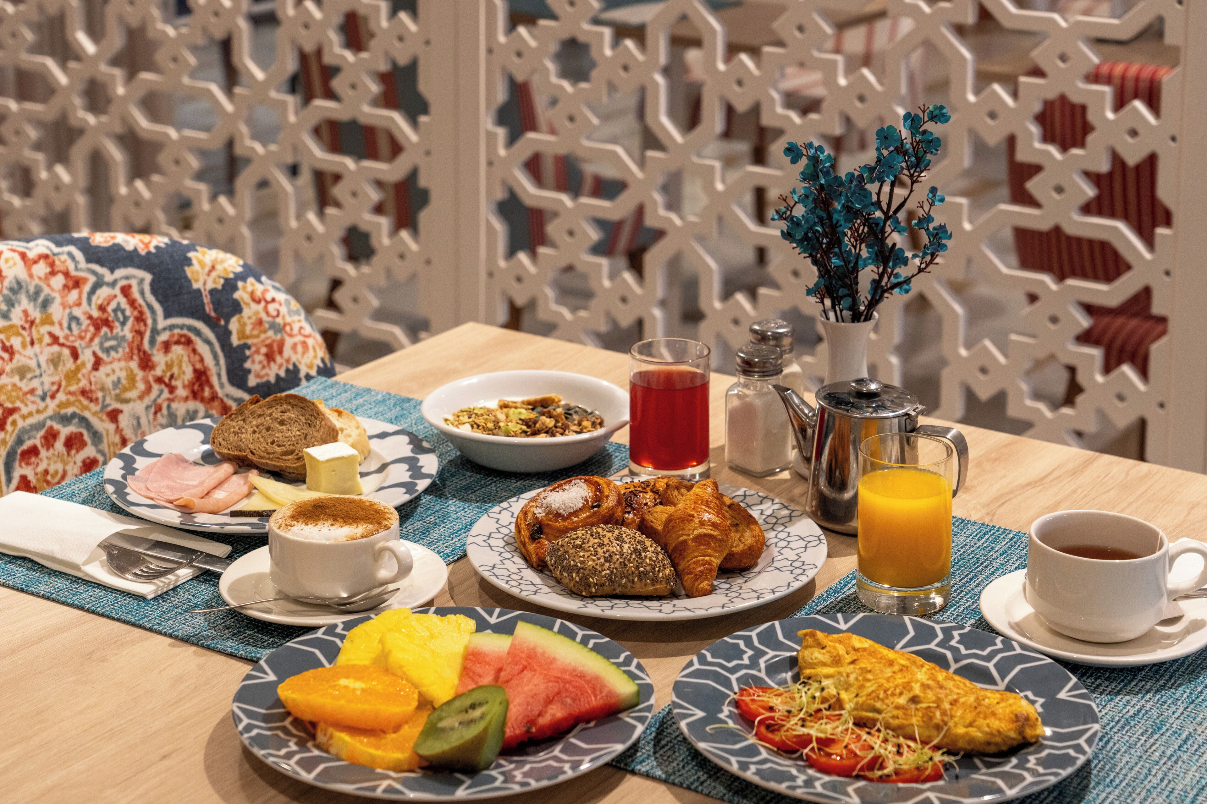 Une table de petit-déjeuner avec divers plats, notamment des toasts, des viennoiseries et des fruits.