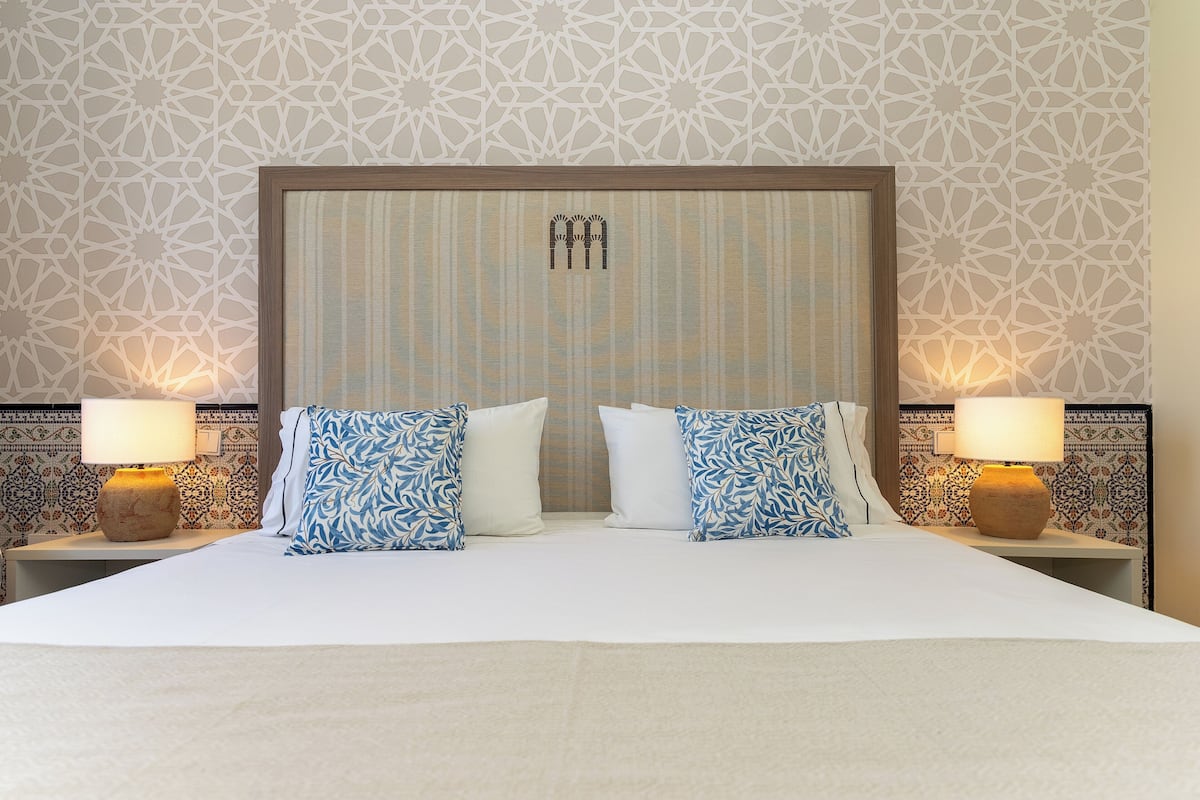 Una habitación de hotel con una cama grande, dos lámparas de noche y un papel tapiz estampado.