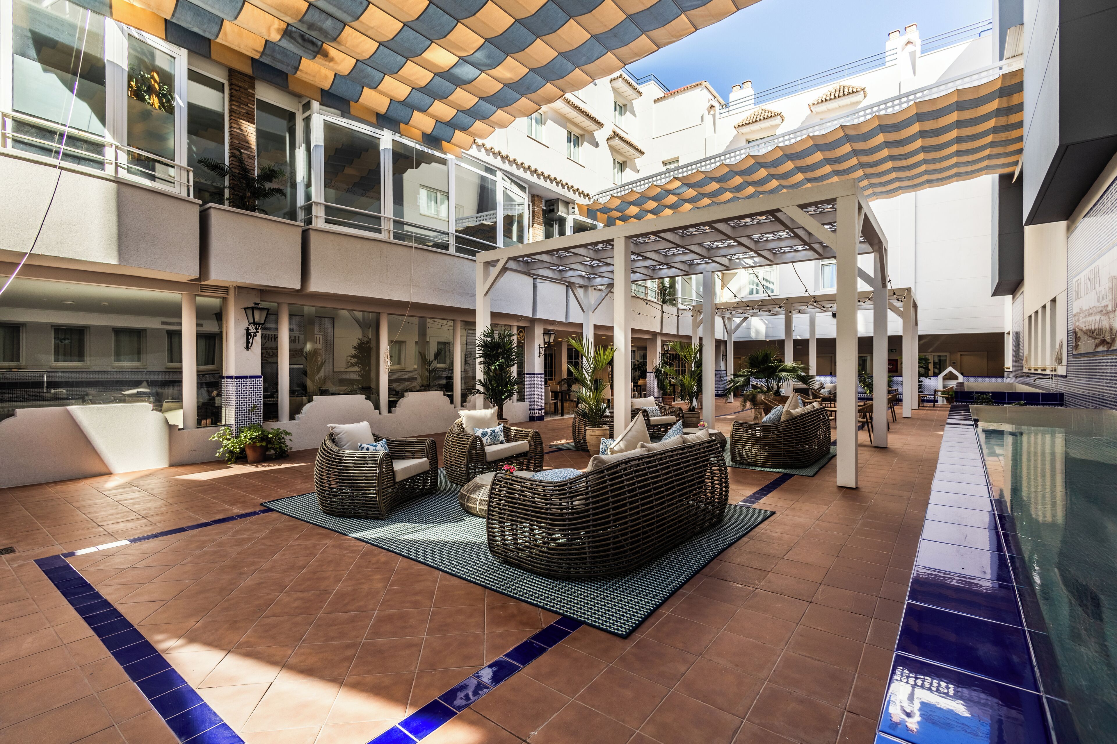 Un amplio patio exterior con varias zonas de estar, una piscina y un paseo cubierto.