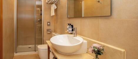 Un baño moderno con un lavamanos grande blanco, una cabina de ducha con paredes de vidrio y un espejo sobre el lavamanos.