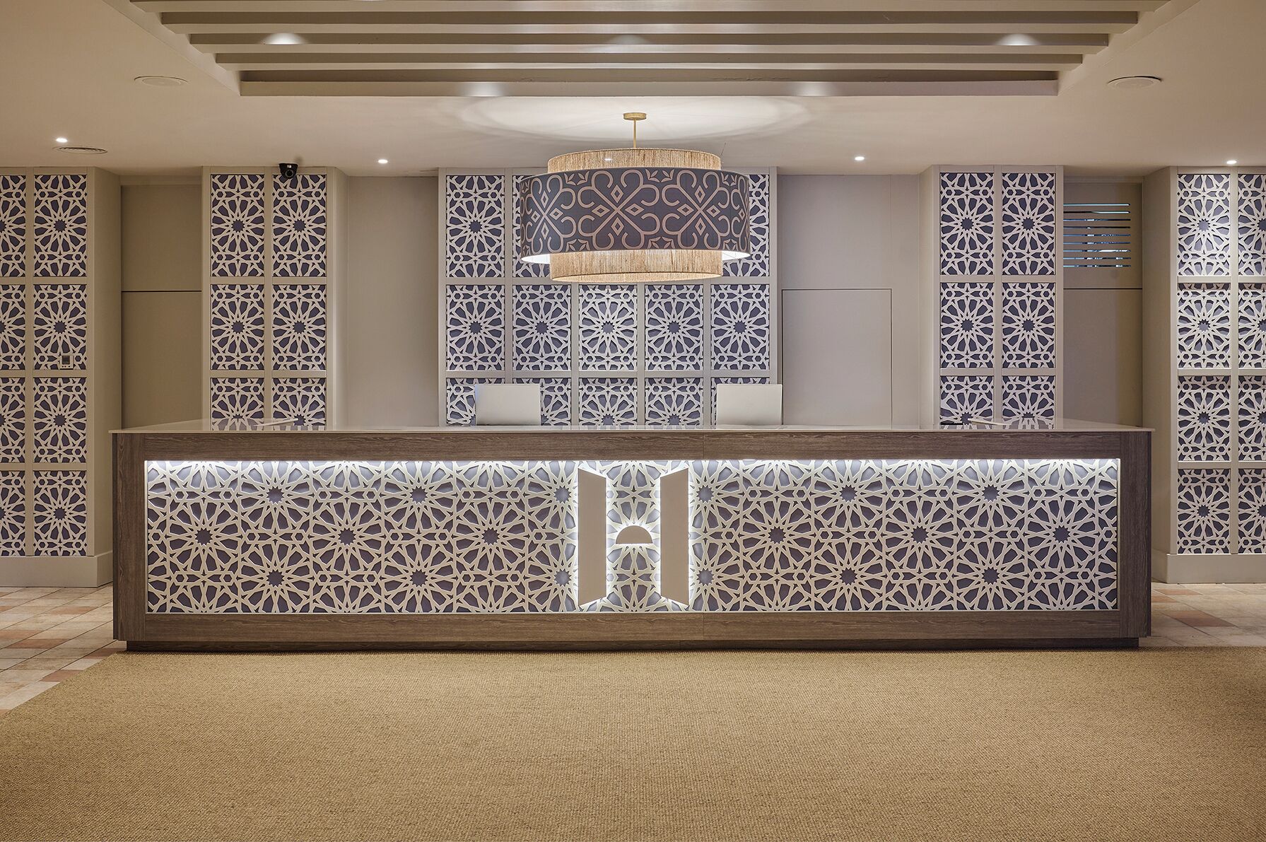 A reception area with a modern design, featuring a central desk with intricate geometric patterns, a chandelier, and decorative panels.