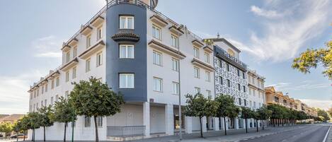 A multi-story hotel with a distinctive corner design, featuring a balcony and a patterned facade.