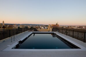 Una piscina infinita en la azotea con vista a la ciudad, rodeada por una valla de metal negro.