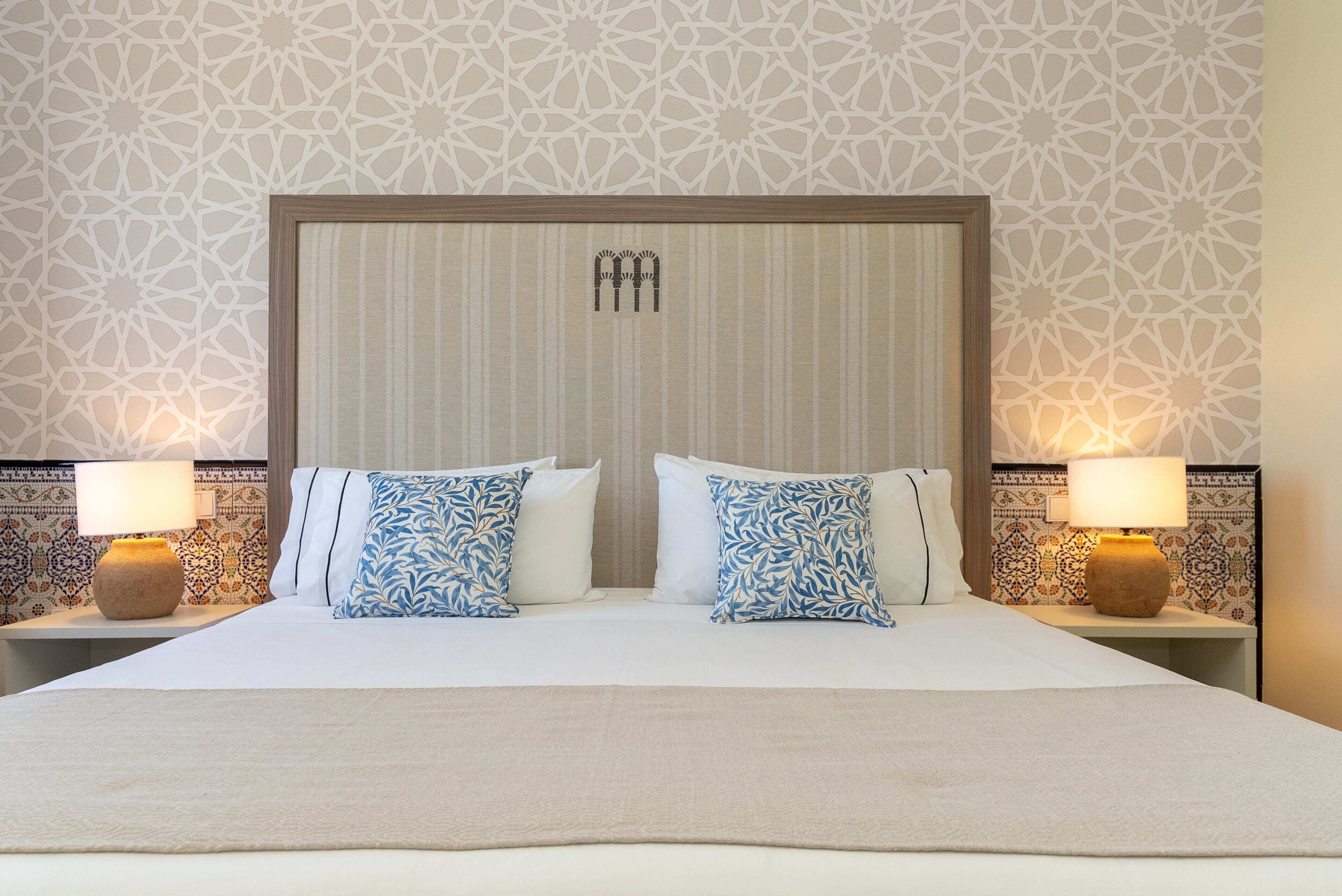 Een hotelkamer met een groot bed, twee nachtkastjes en behang met een patroon.