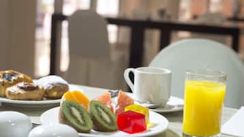 Un desayuno con pasteles, fruta, una taza y un vaso de zumo de naranja sobre una mesa.