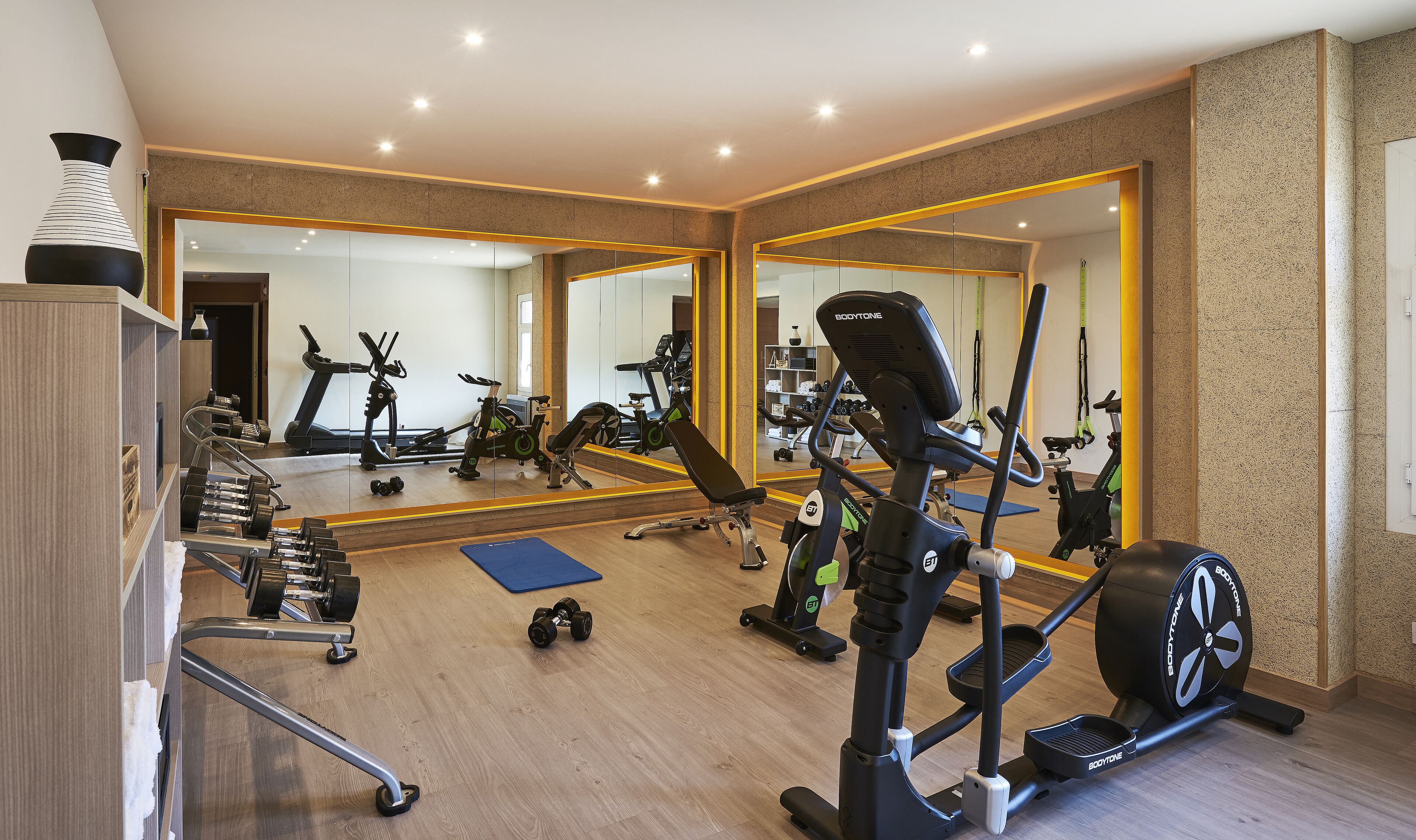 A modern gym with various exercise equipment, a large mirror, and a wooden floor.
