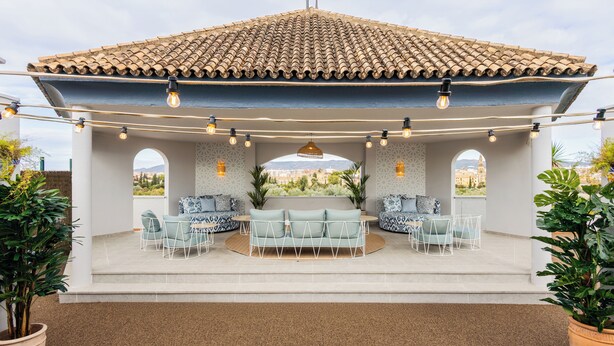 An outdoor patio with a tiled roof, seating area, and potted plants.