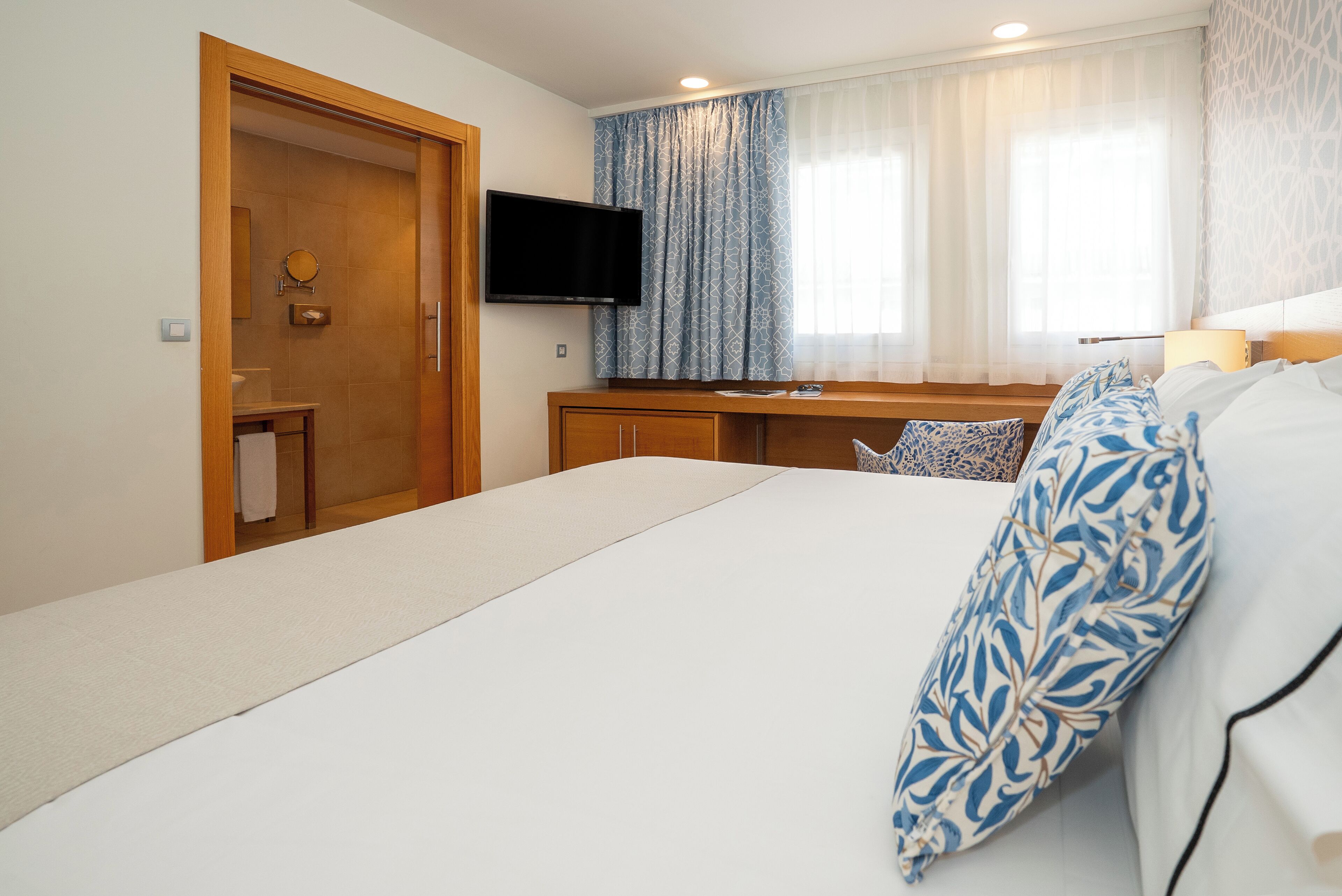 Habitación de hotel con cama, televisión, escritorio y ventana con cortinas.
