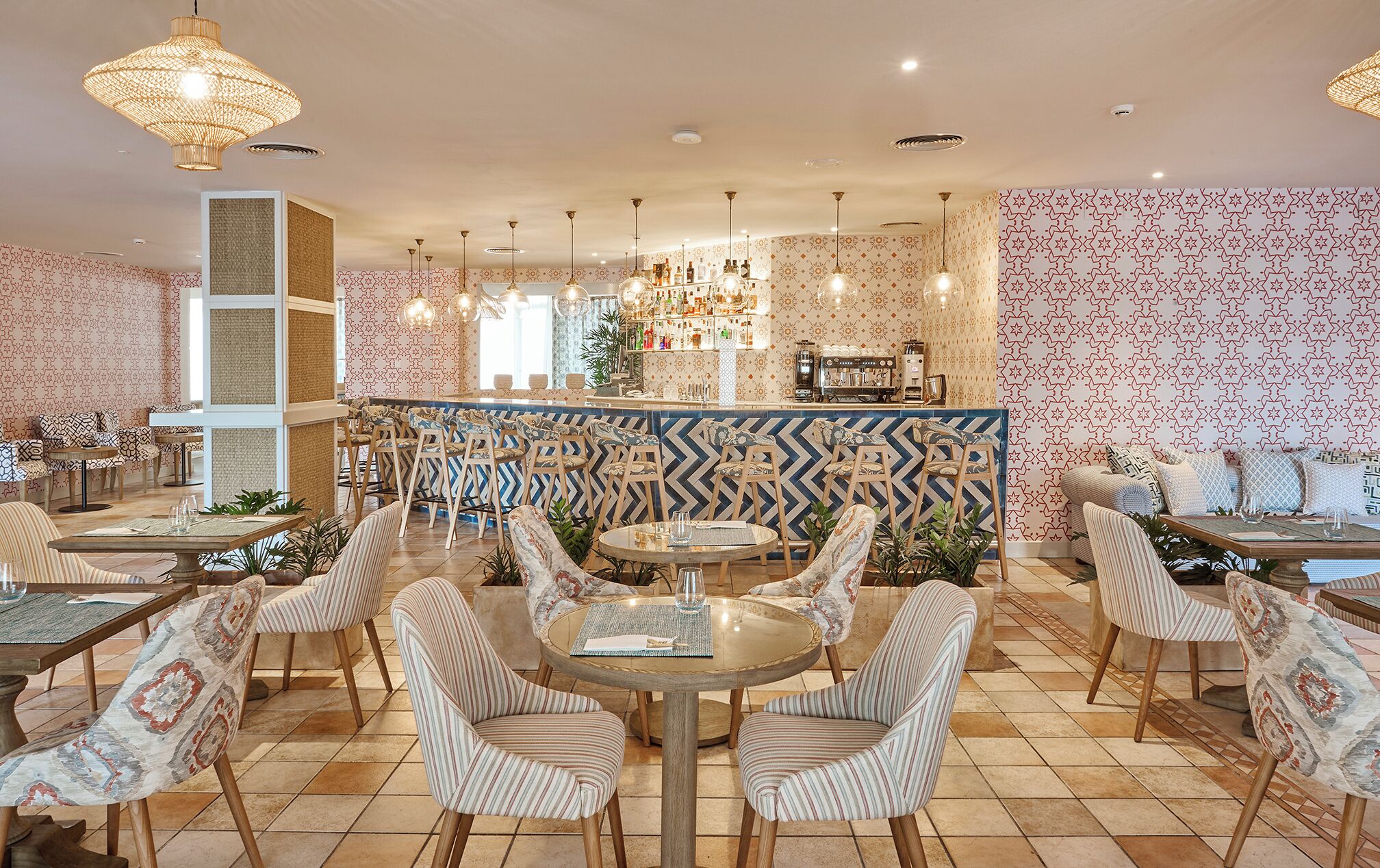 A restaurant with a bar area, striped chairs, and patterned wallpaper.