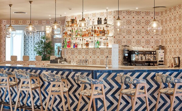 Uma área de bar com parede estampada, uma máquina de café e banquetas.