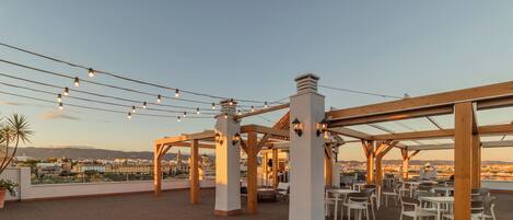 A rooftop terrace with string lights, wooden pergolas, and outdoor seating.