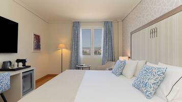 Une chambre d’hôtel avec un grand lit, un bureau avec une machine à café, une chaise, un téléviseur fixé au mur et une fenêtre avec des rideaux.