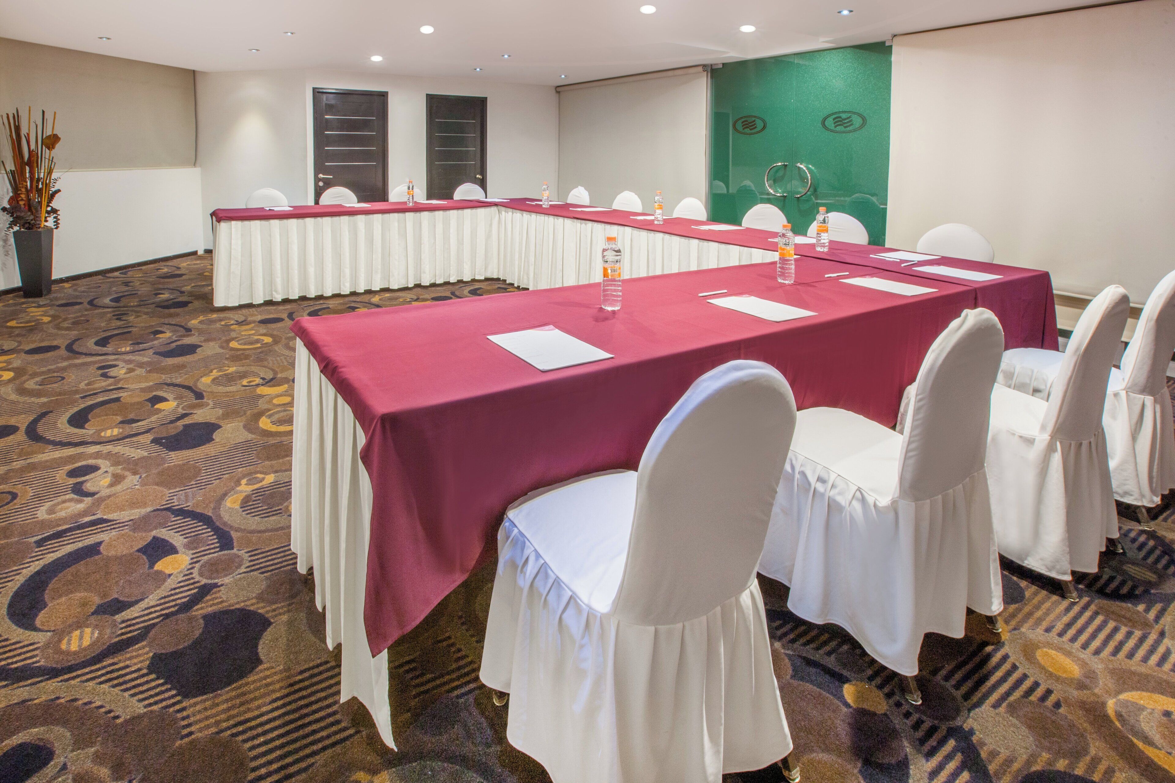 A conference room with long tables, white chairs, and a patterned carpet.
