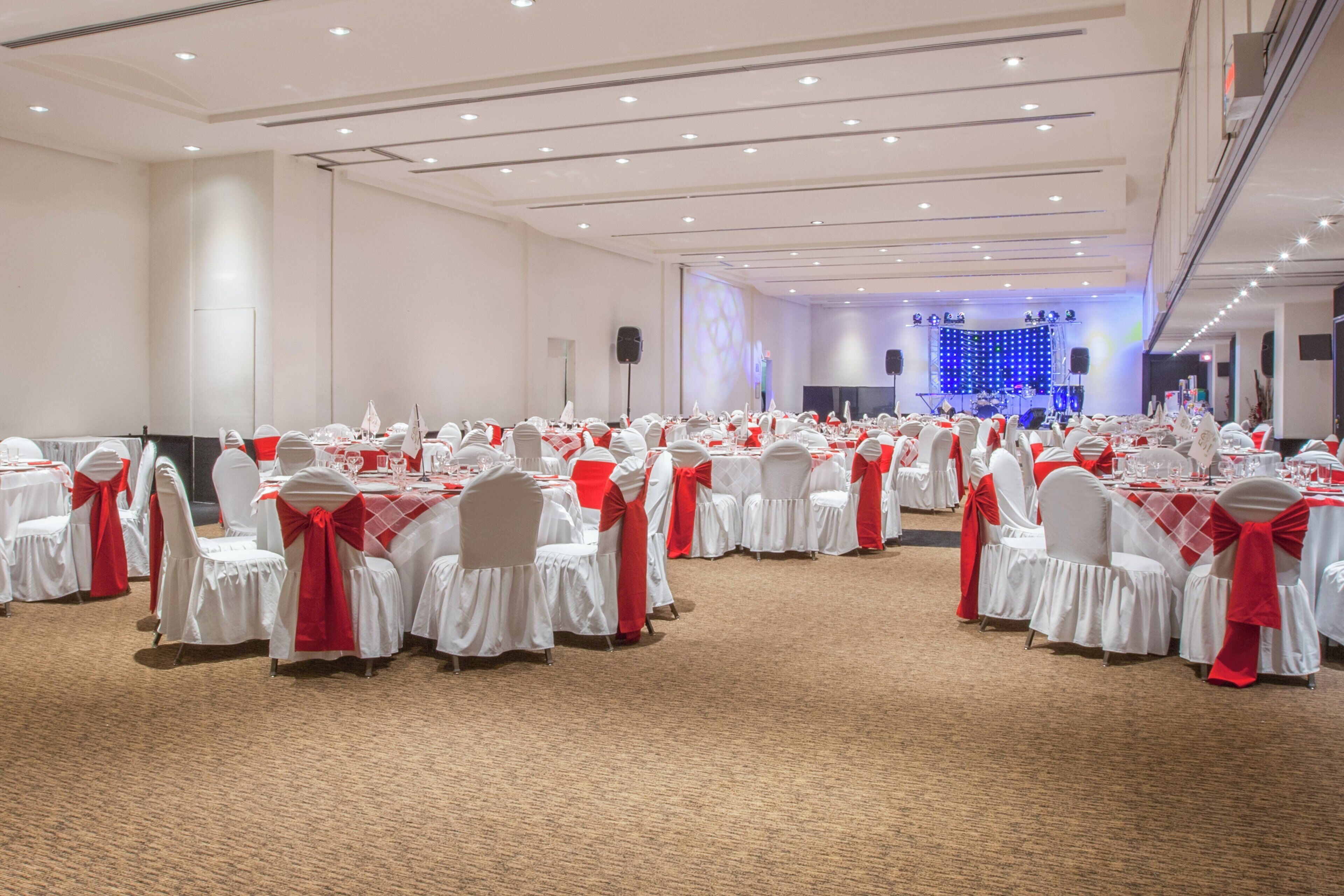 Une salle de banquet avec des tables rondes, des chaises blanches et des rubans rouges.