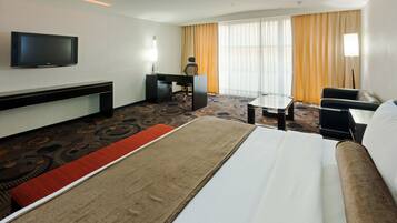 A hotel room with a bed, a desk, a chair, a TV, and a large window with curtains.