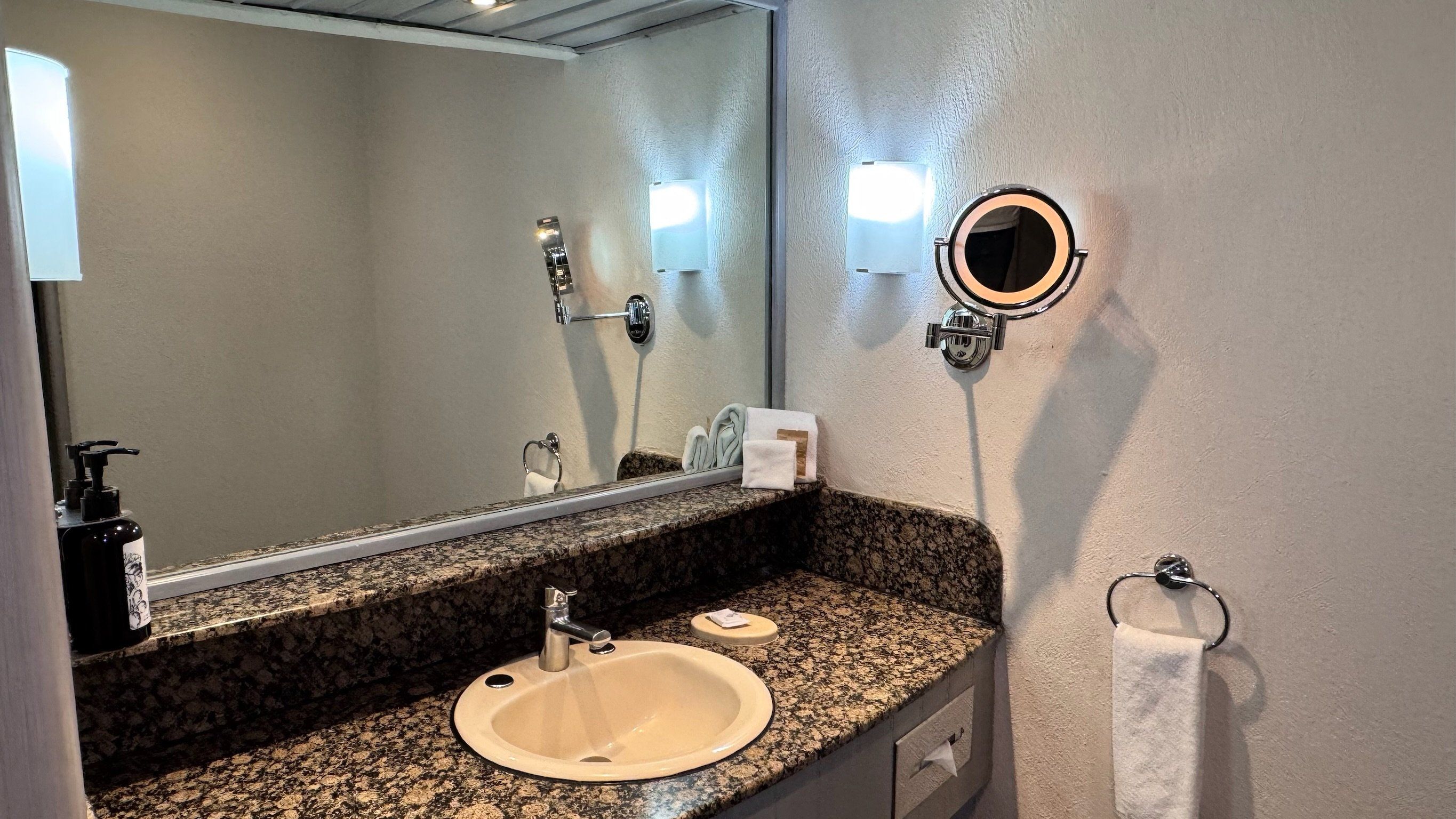 A bathroom with a granite countertop, a sink, a mirror, a towel rack, and a toilet paper holder.