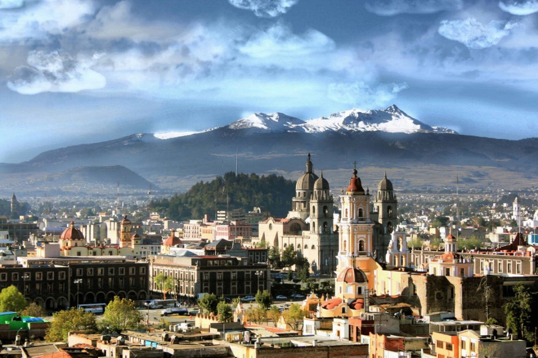 Un paisaje urbano con una iglesia destacada y una montaña nevada al fondo.