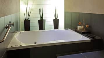 Un baño moderno con una bañera independiente, tres plantas en macetas y una mesita con una vela y objetos decorativos.