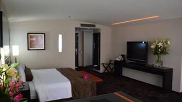 A hotel room with a bed, a desk, a television, and a vase of flowers.