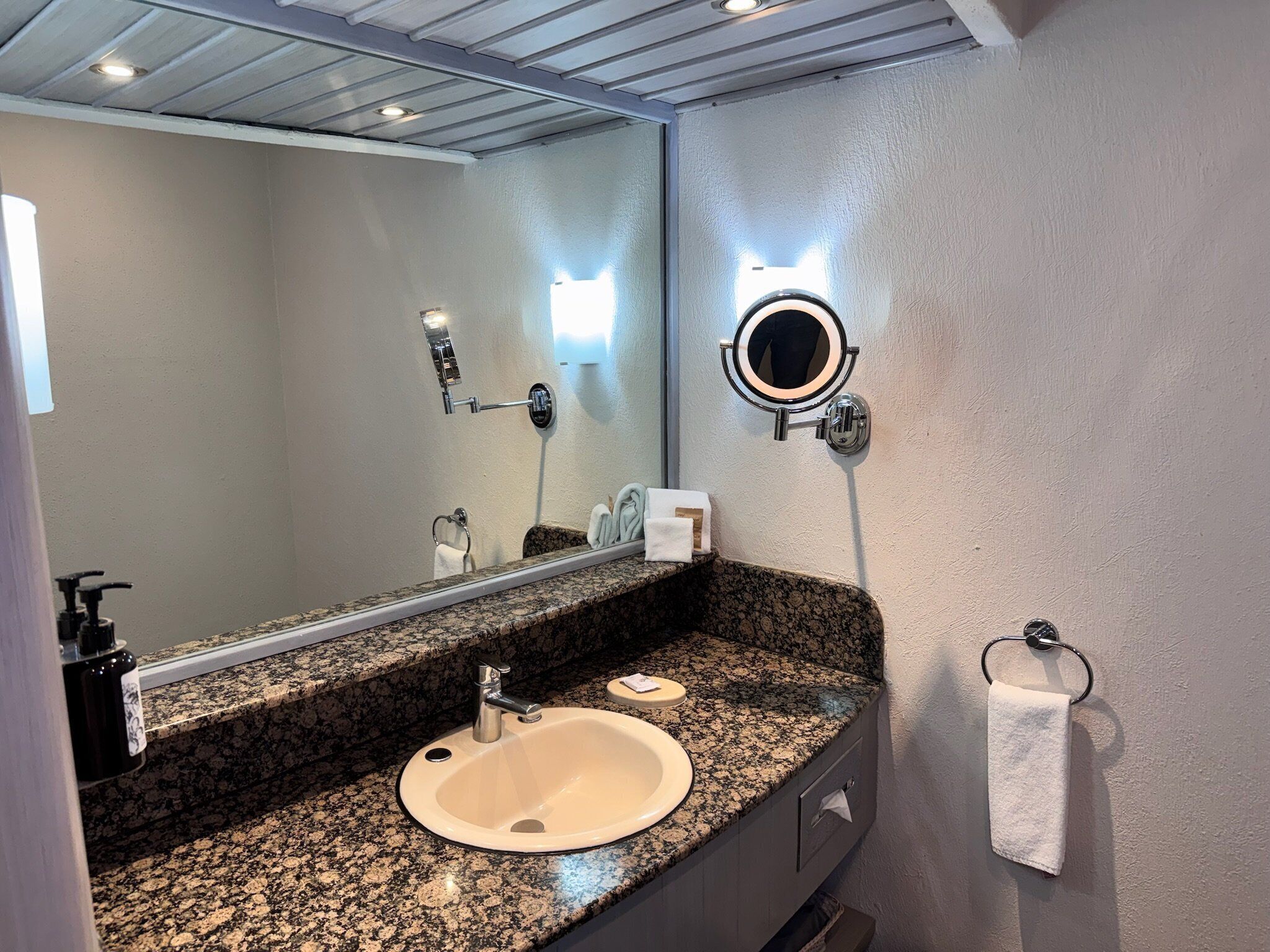 A bathroom with a granite countertop, a sink, a mirror with a light, and a towel rack.