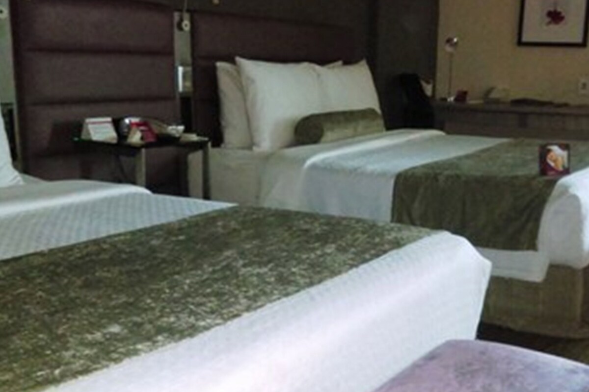 A hotel room with two beds, a nightstand, and a small table with a lamp.