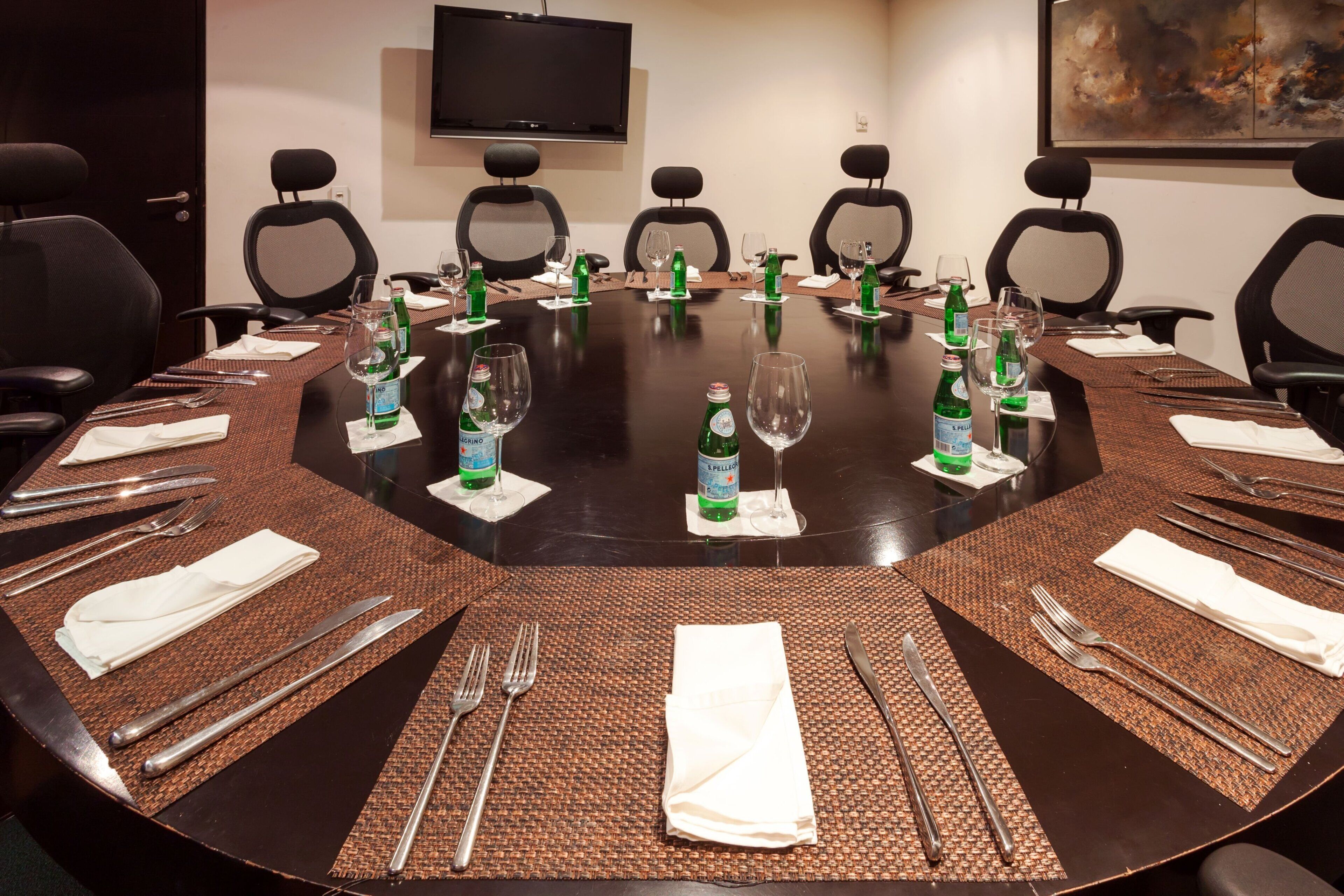 A conference room with a round table, chairs, and a TV mounted on the wall.
