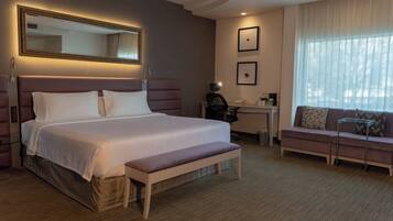 A hotel room with a large bed, a desk, a chair, a bench, and a sofa.