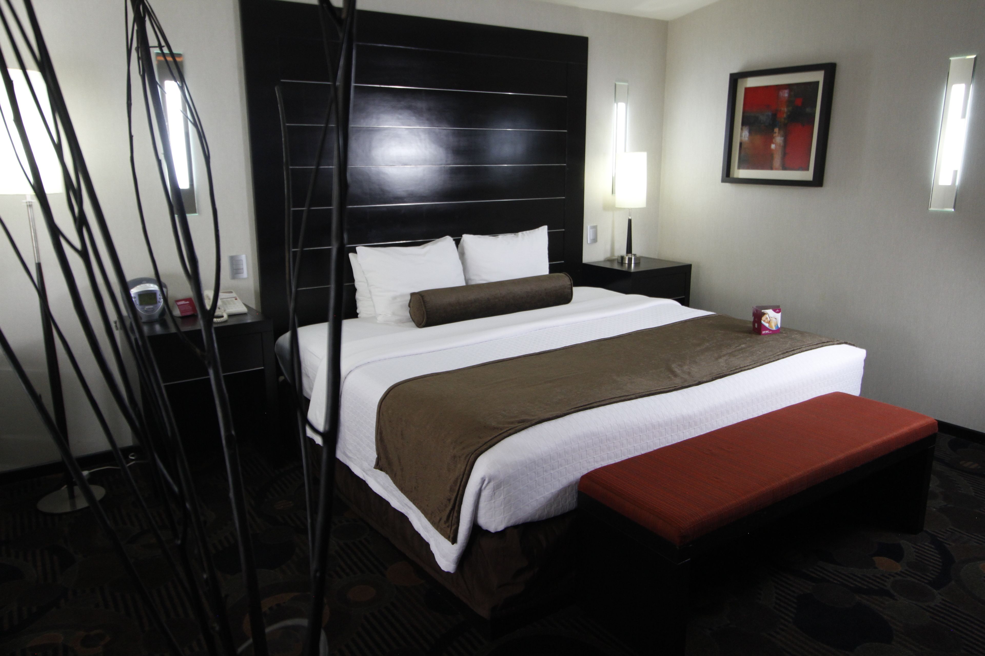 Habitación de hotel con una cama grande, una mesita de noche, un banco y una lámpara de pared.