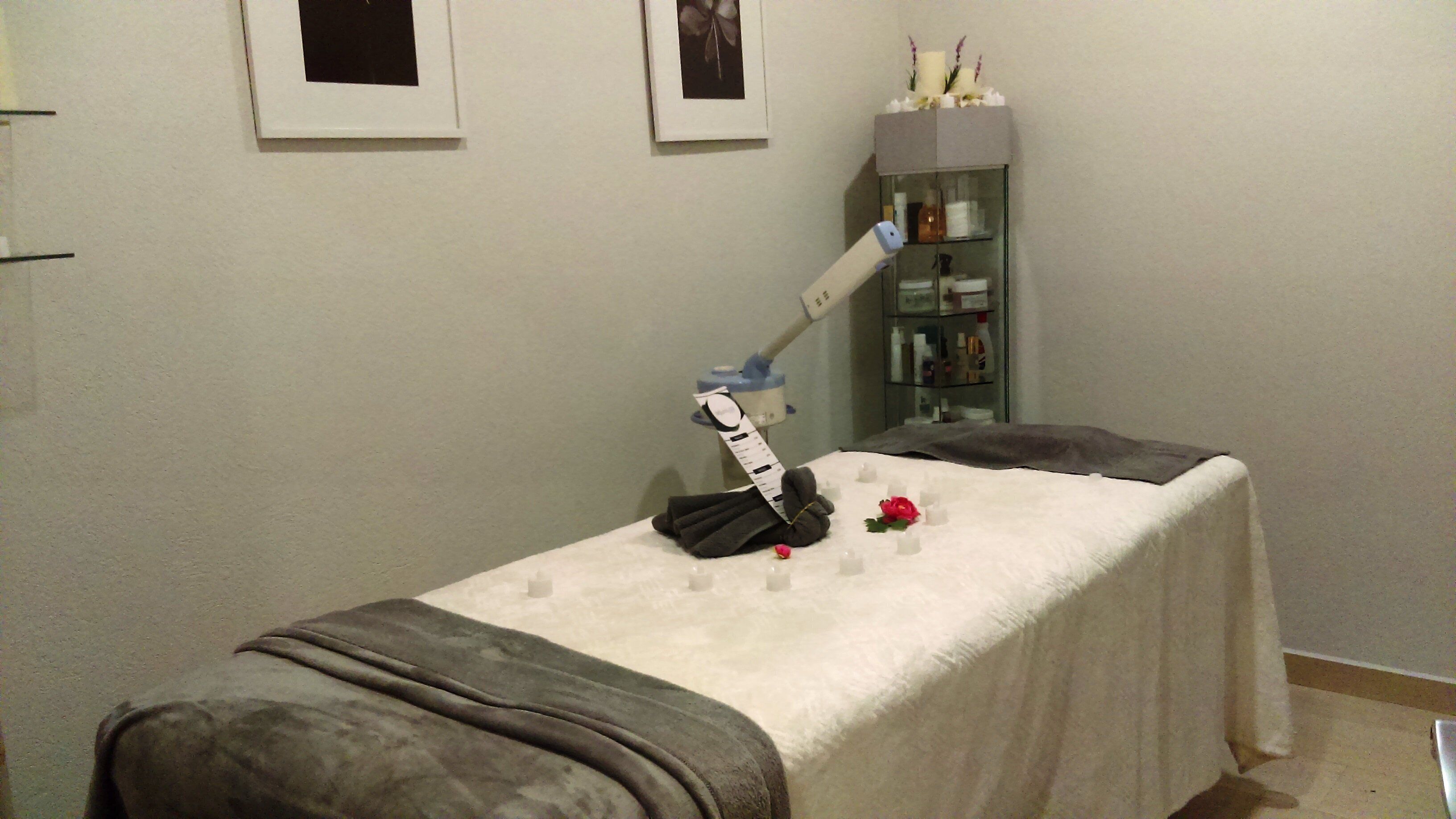 A room with a massage table, a shelf with toiletries, and framed pictures on the wall.