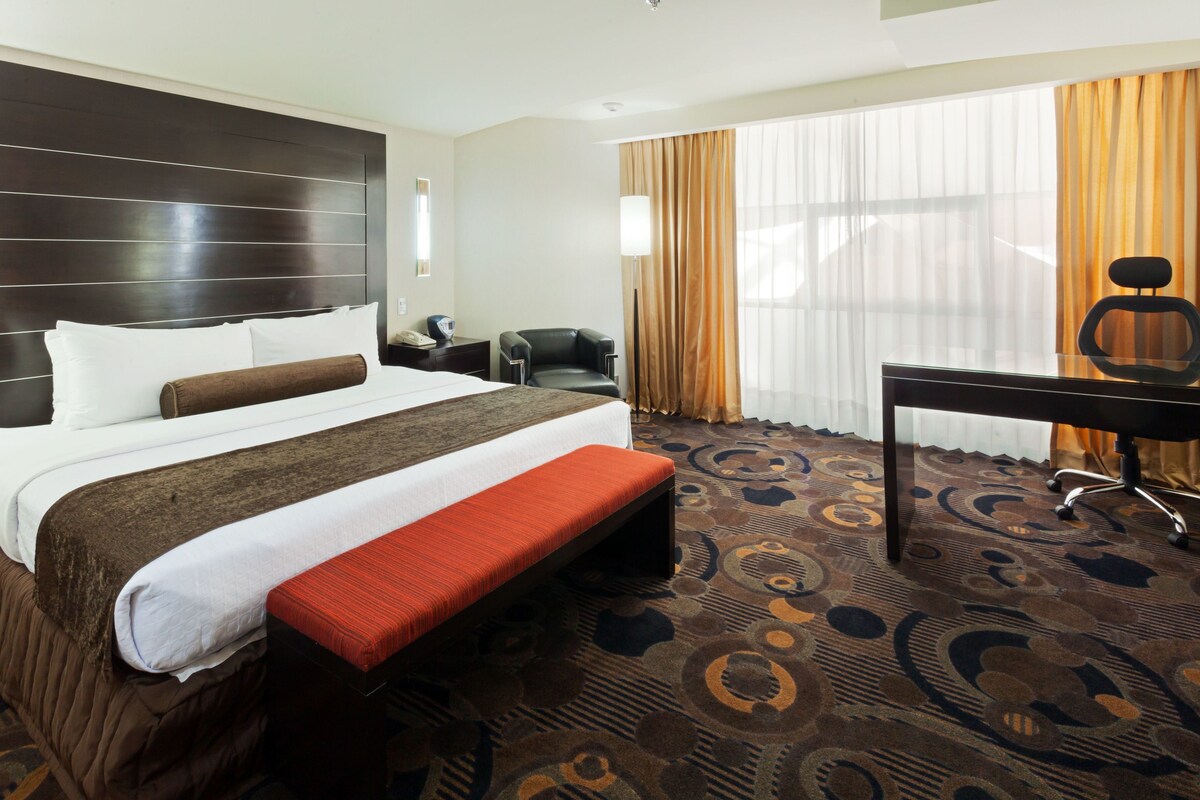 A hotel room with a large bed, a desk, a chair, and a patterned carpet.