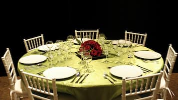 Una mesa redonda dispuesta para una comida, con sillas blancas, mantel verde y un centro de mesa con rosas rojas.