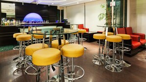 Zona de bar con taburetes y una mesa de vidrio, rodeada de asientos rojos y amarillos.