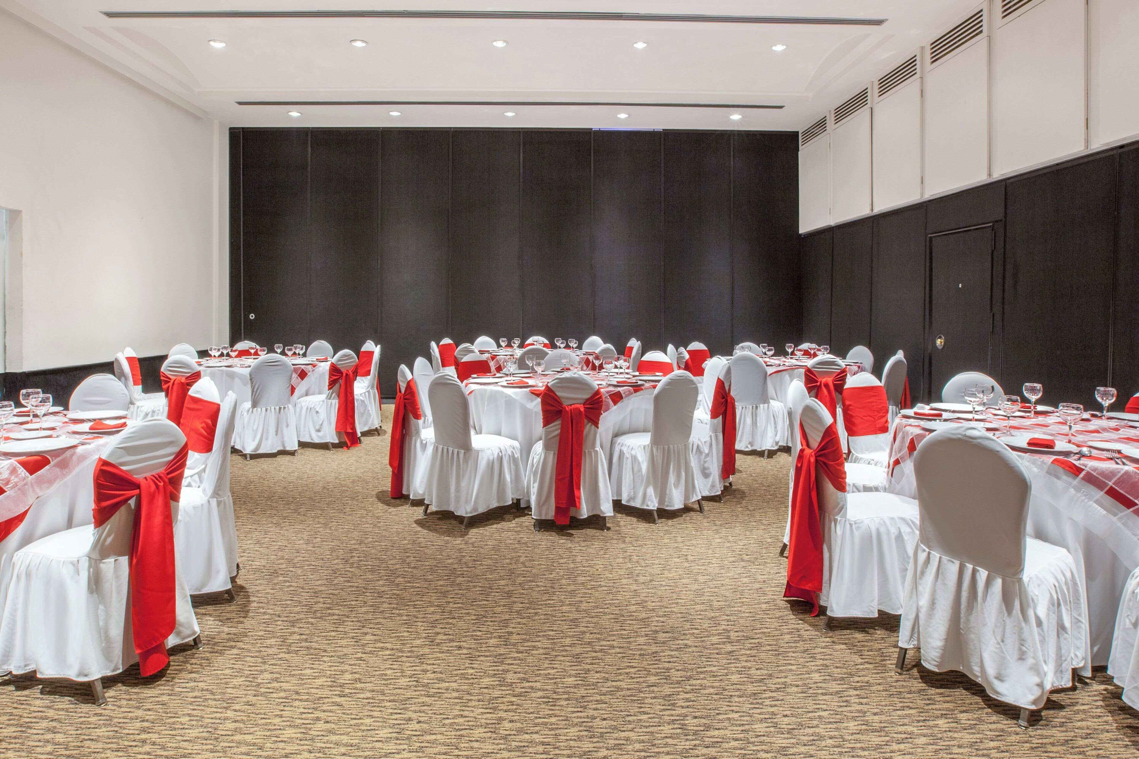 A conference room with round tables, white chairs, and red sashes.