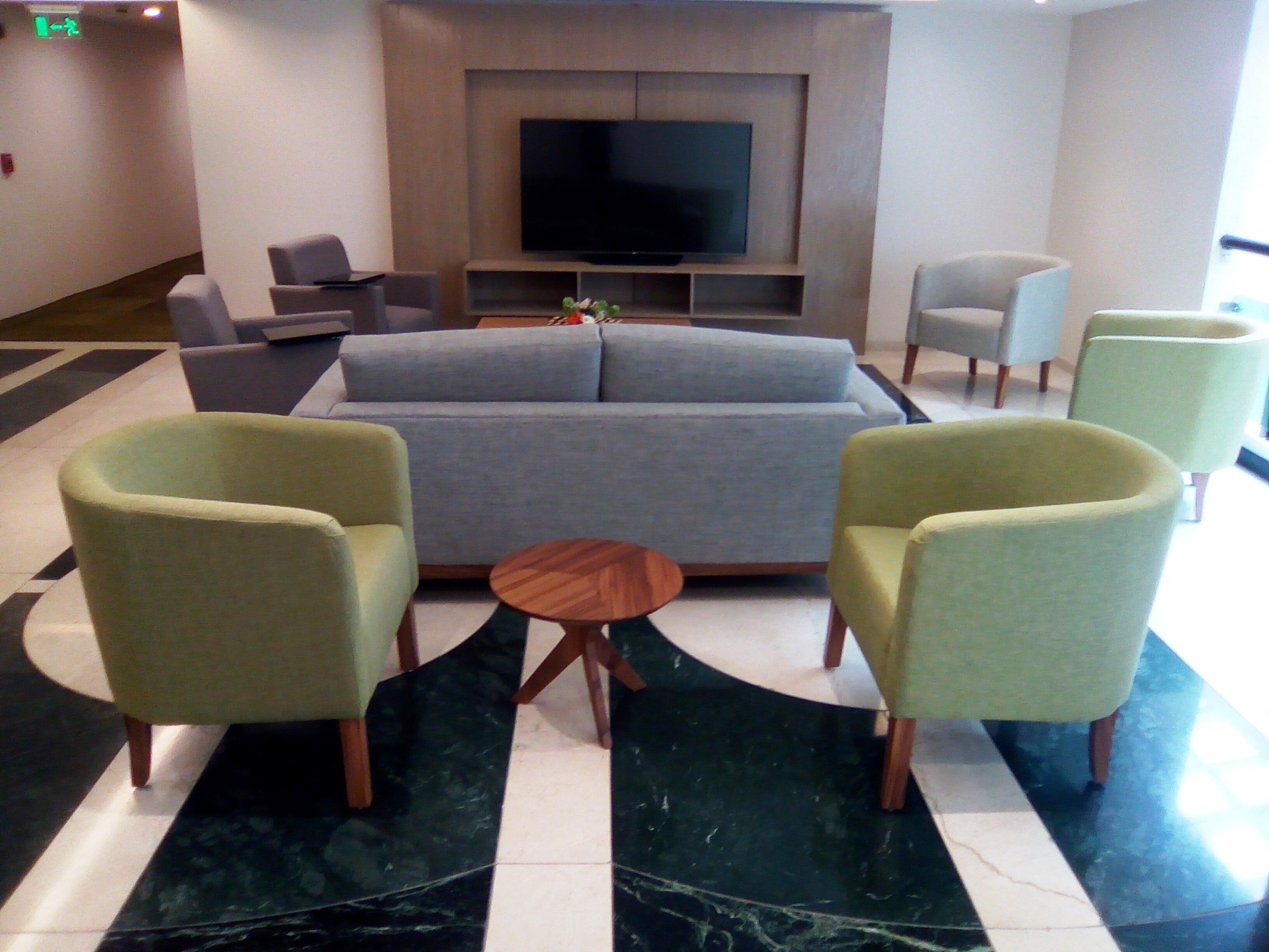 A modern living area with a sofa, armchairs, a coffee table, and a flat-screen TV mounted on a wall.