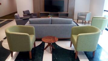 Un área de estar moderna con un sofá, sillones, una mesa de centro y un televisor de pantalla plana montado en la pared.