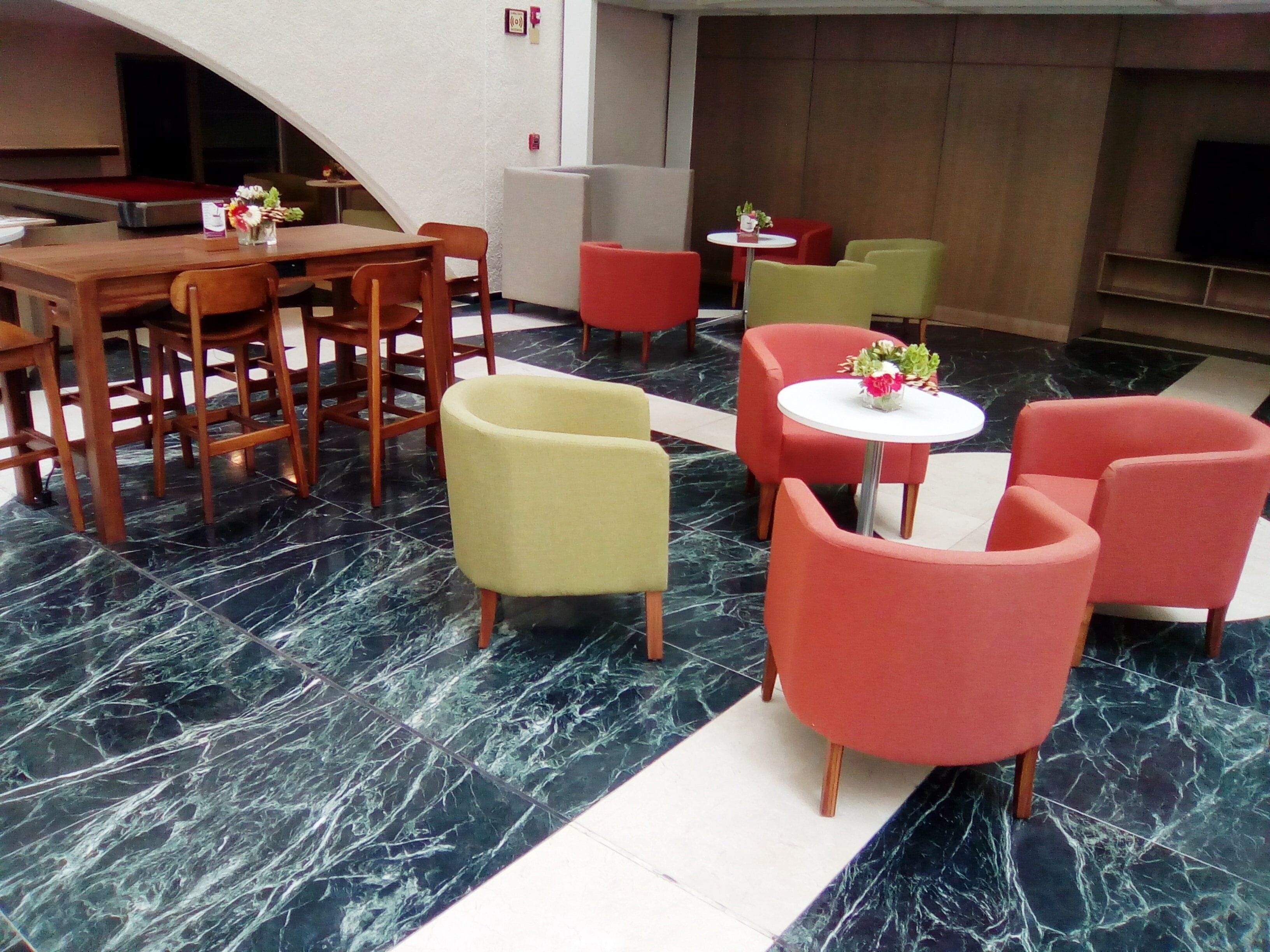 A lobby with a pool table, wooden chairs, and red and yellow sofas.