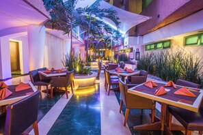 Un vestíbulo de hotel con una zona de estar central, un mostrador de recepción y una escalera que conduce a los pisos superiores.