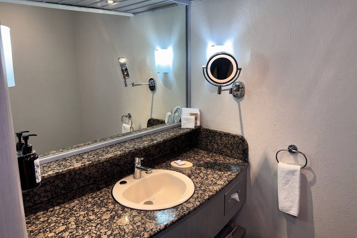 A bathroom with a granite countertop, a sink, a mirror with a light, and a towel rack.