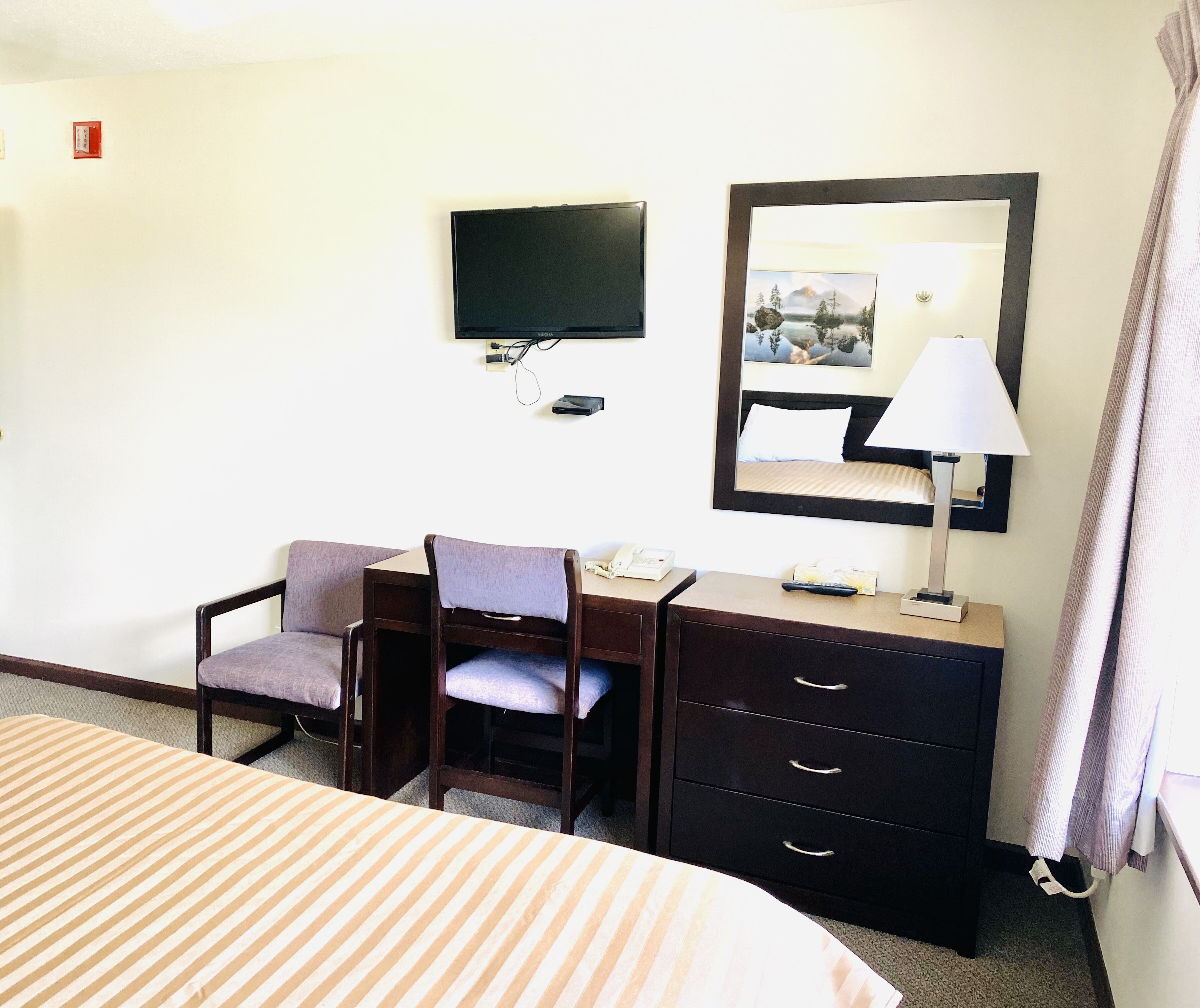 Une chambre d’hôtel comprenant un lit, un bureau avec une chaise, une télévision, un miroir et une lampe.
